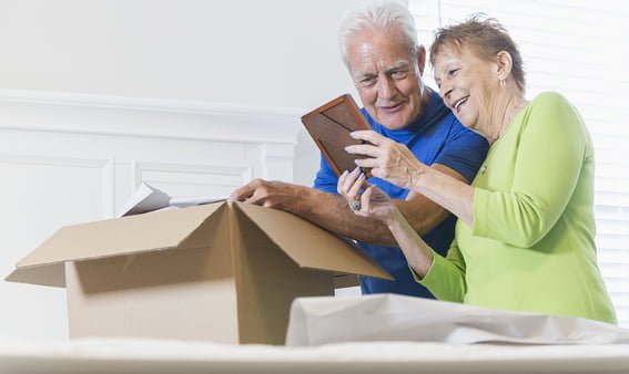 Pareja mayor empaquetando una caja, mirando un marco